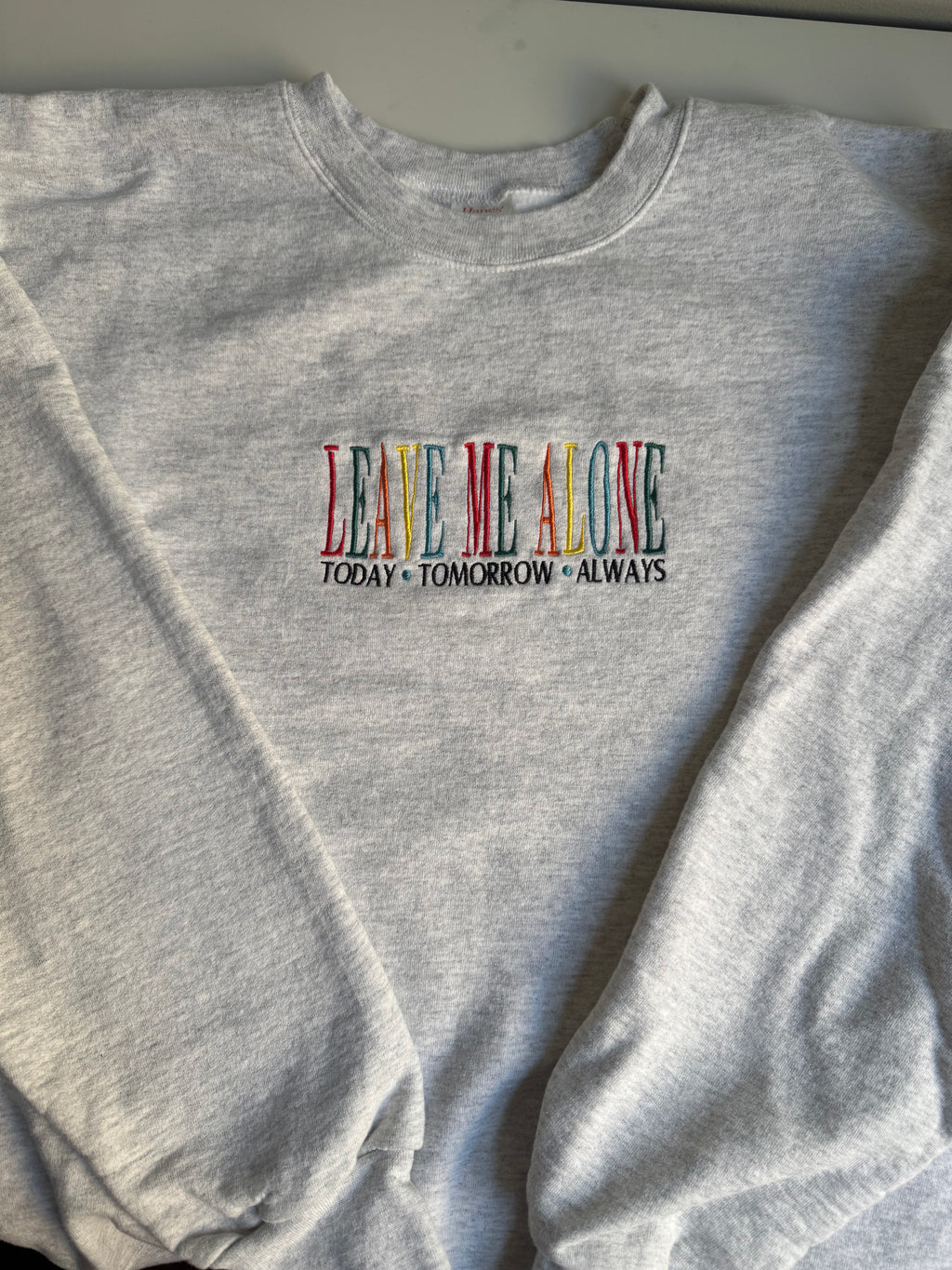 Gray sweatshirt with colorful text 'LEAVE ME ALONE TODAY TOMORROW ALWAYS' on a plain background