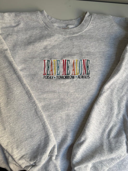 Gray sweatshirt with colorful text 'LEAVE ME ALONE TODAY TOMORROW ALWAYS' on a plain background